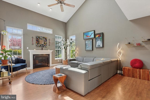 living room with a fireplace, high vaulted ceiling, ceiling fan, baseboards, and wood finished floors