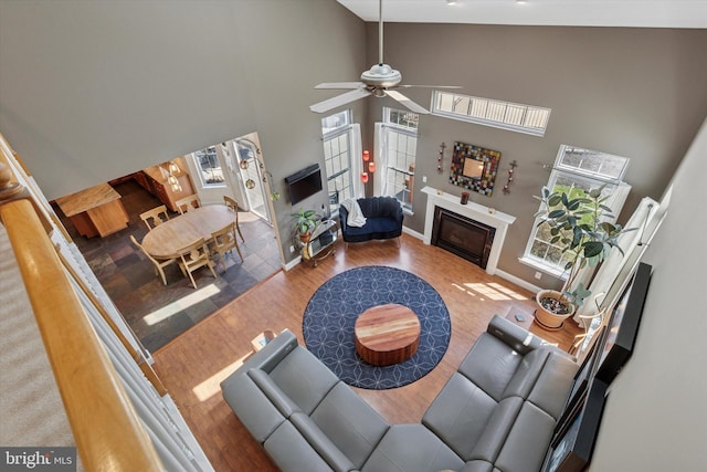 living area with ceiling fan, baseboards, a glass covered fireplace, wood finished floors, and high vaulted ceiling