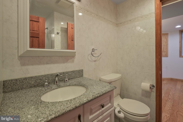 full bathroom with tile walls, toilet, vanity, and a shower with door