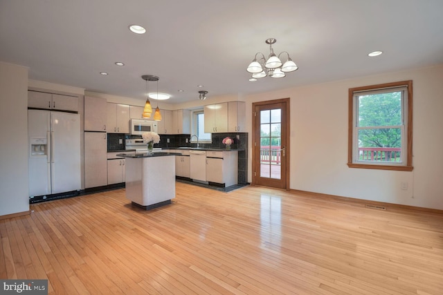 kitchen with white appliances, dark countertops, a sink, a chandelier, and light wood finished floors