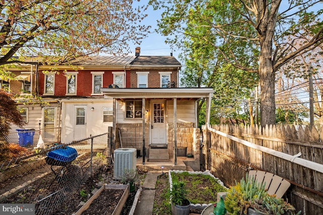 back of house with brick siding, central AC unit, a fenced backyard, and a garden