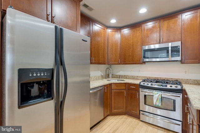 kitchen with a sink, stainless steel appliances, light wood finished floors, light stone countertops, and visible vents