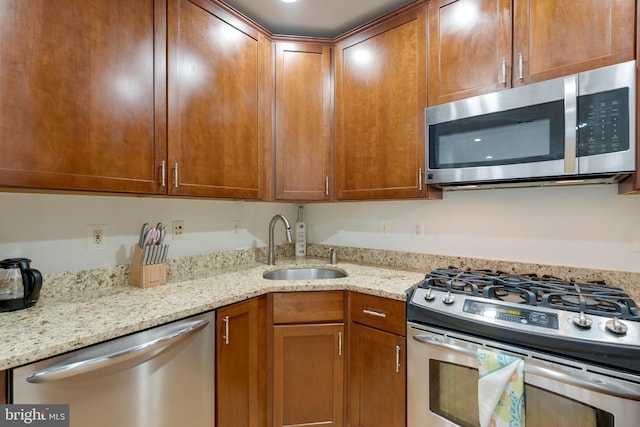 kitchen with brown cabinets, appliances with stainless steel finishes, light stone countertops, and a sink