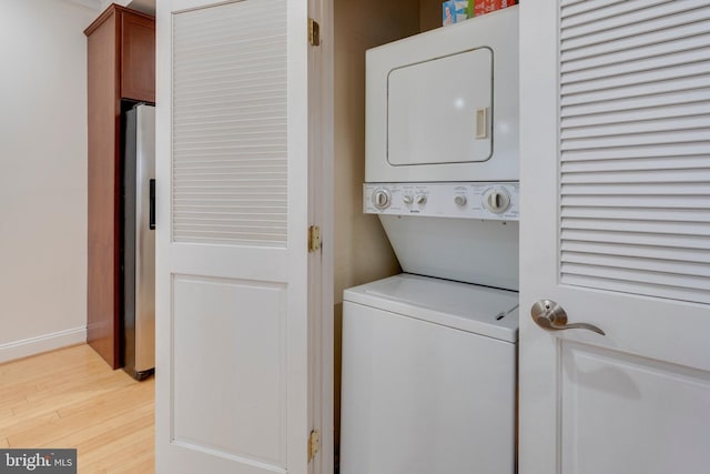 laundry area with baseboards, stacked washer / drying machine, light wood-style floors, and laundry area