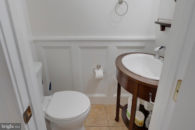 half bath with wainscoting, toilet, and a decorative wall