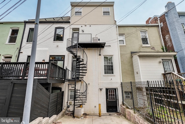 rear view of property with brick siding, central AC unit, fence, and stairs