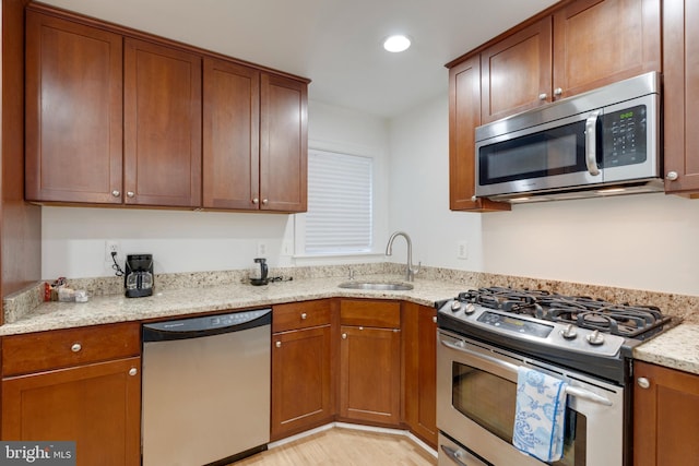 kitchen with light stone counters, a sink, brown cabinetry, appliances with stainless steel finishes, and recessed lighting
