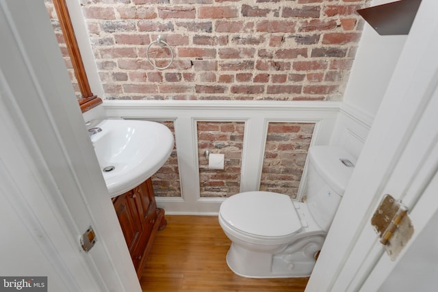 bathroom featuring a decorative wall, vanity, brick wall, a wainscoted wall, and toilet