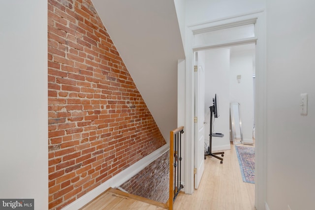 hallway with brick wall, lofted ceiling, an upstairs landing, and light wood-style floors