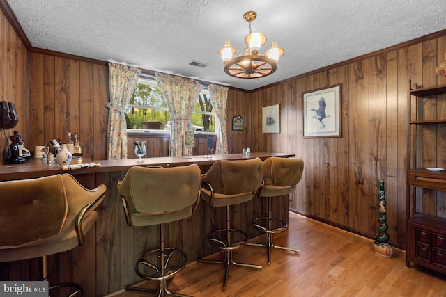 bar area featuring a chandelier, a textured ceiling, wood finished floors, wooden walls, and crown molding