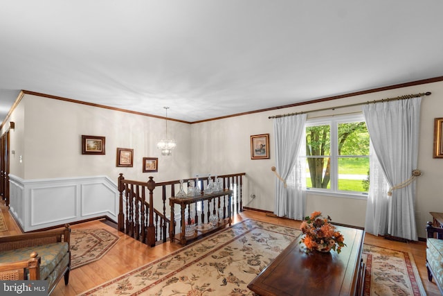 living area featuring a chandelier, light wood finished floors, crown molding, and a wainscoted wall