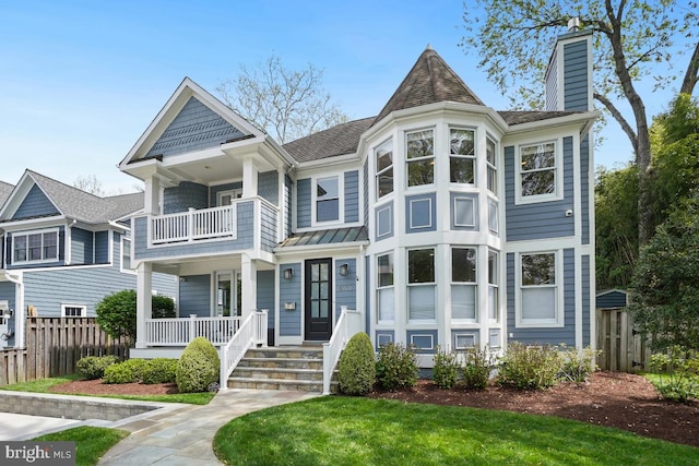 victorian-style house featuring fence, a balcony, a chimney, and covered porch