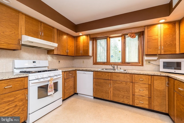 kitchen with brown cabinets, white appliances, under cabinet range hood, and a sink