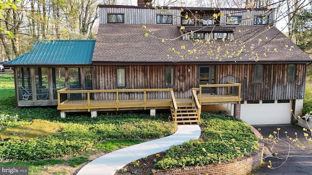 back of house featuring a garage, a shingled roof, driveway, and a sunroom