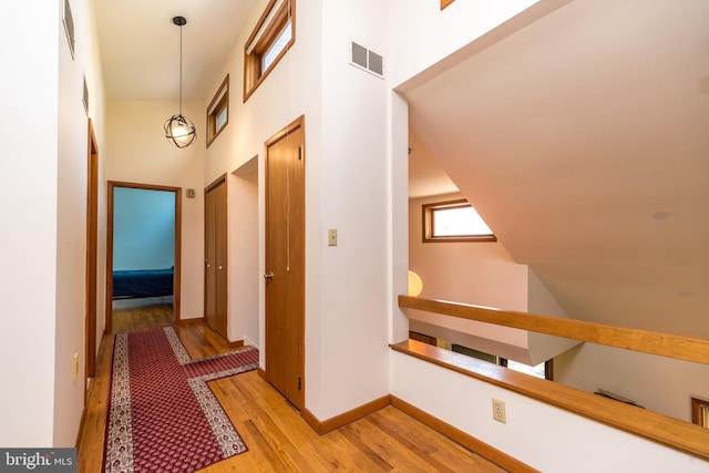 hall with visible vents, a high ceiling, light wood-style flooring, and an upstairs landing
