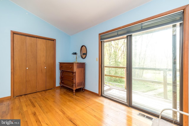 unfurnished bedroom featuring a closet, access to outside, light wood-type flooring, baseboards, and lofted ceiling