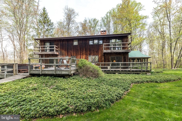rear view of property featuring a wooden deck, a yard, and a chimney