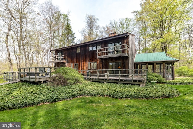 rear view of house featuring a deck, a chimney, metal roof, and a lawn