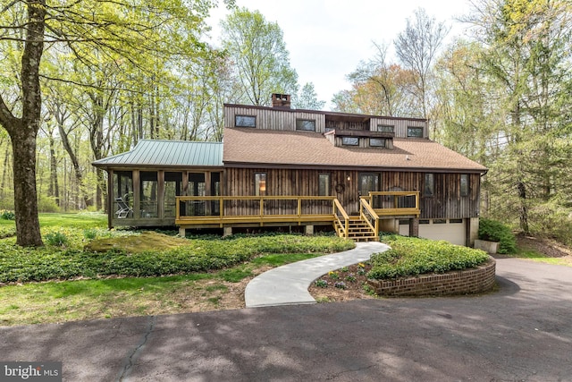 view of front facade with a chimney, aphalt driveway, a sunroom, and an attached garage