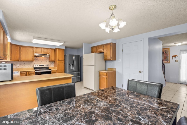 12916 New Hampshire Ave, Silver Spring, MD 20904 - kitchen with appliances with stainless steel finishes, under cabinet range hood, a textured ceiling, light tile patterned floors, and a chandelier