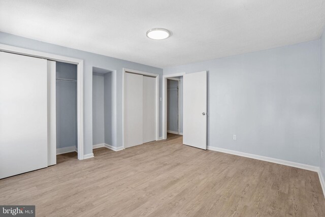 unfurnished bedroom with wood finished floors, multiple closets, and baseboards