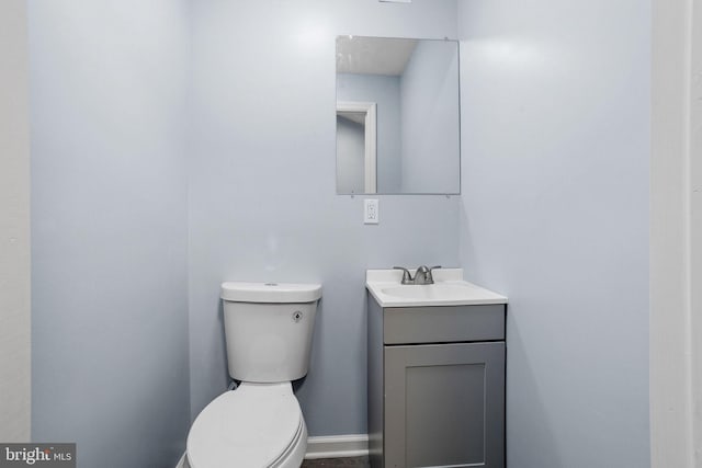 half bath with baseboards, toilet, and vanity
