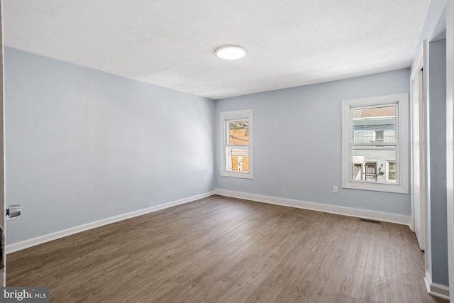 empty room with baseboards, visible vents, and dark wood-style floors