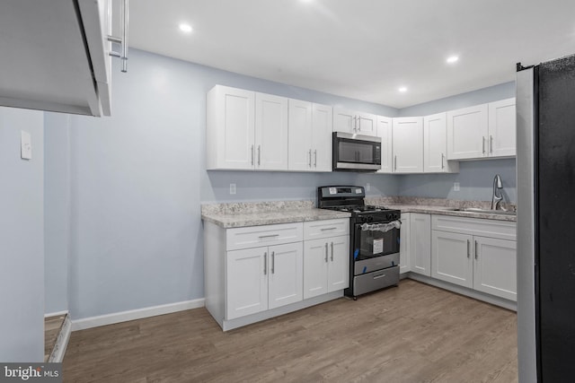 kitchen featuring a sink, light wood-type flooring, stainless steel appliances, white cabinets, and baseboards