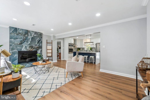 living area with a stone fireplace, light wood-type flooring, baseboards, ornamental molding, and recessed lighting
