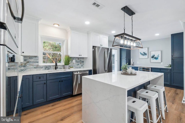 kitchen featuring decorative backsplash, blue cabinetry, a kitchen bar, a sink, and stainless steel appliances
