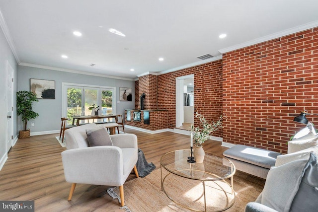 living room with brick wall, baseboards, wood finished floors, visible vents, and ornamental molding