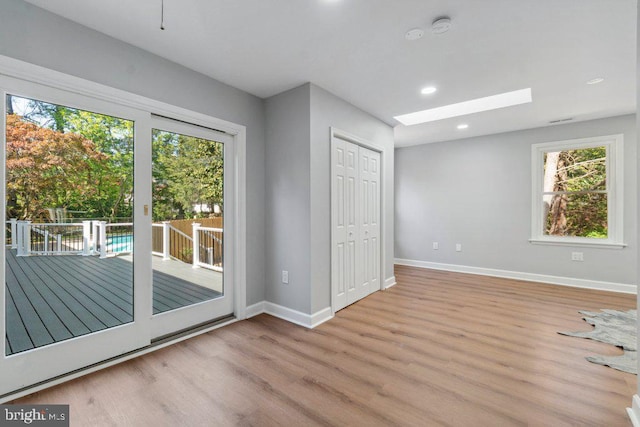 interior space featuring access to outside, recessed lighting, baseboards, wood finished floors, and a skylight