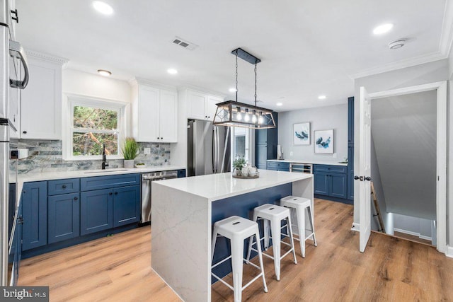 kitchen featuring a sink, stainless steel appliances, a kitchen bar, visible vents, and blue cabinets
