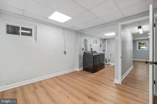 basement featuring a paneled ceiling, baseboards, washer and clothes dryer, and light wood-style flooring