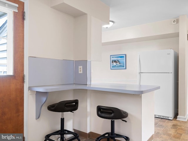kitchen featuring freestanding refrigerator, stone finish floor, a wealth of natural light, and a breakfast bar area