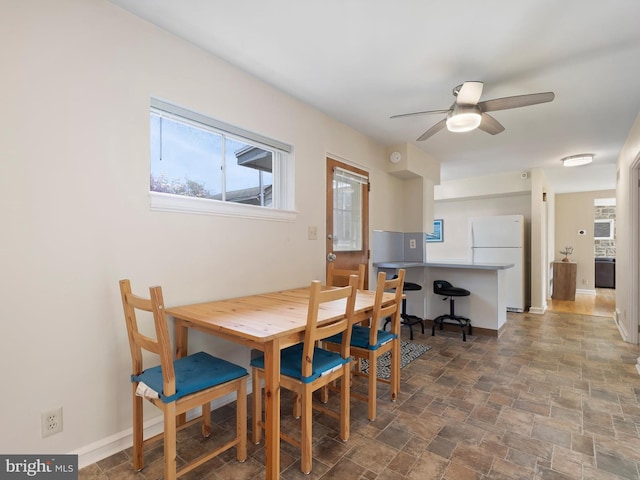 dining space featuring baseboards, a ceiling fan, and stone finish floor