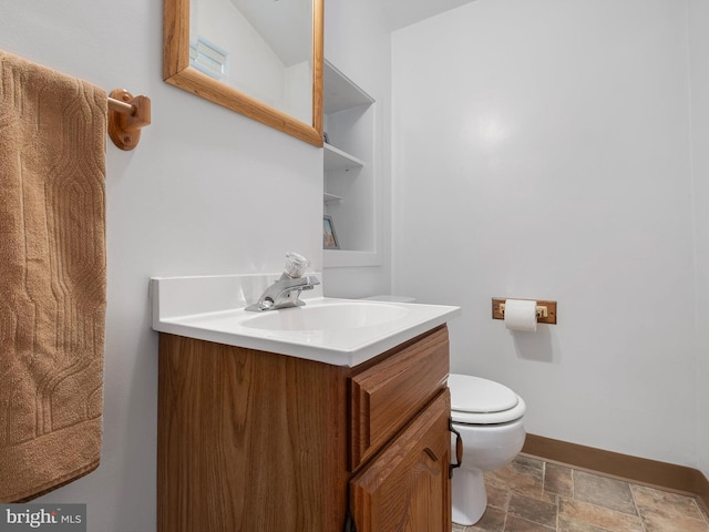bathroom with vanity, baseboards, stone finish floor, and toilet