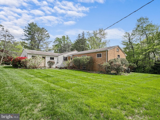 rear view of property featuring cooling unit, a yard, and brick siding