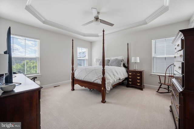 bedroom featuring a tray ceiling, crown molding, multiple windows, baseboards, and light carpet