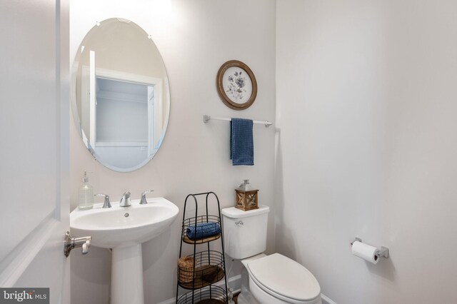 half bathroom featuring toilet, baseboards, and a sink