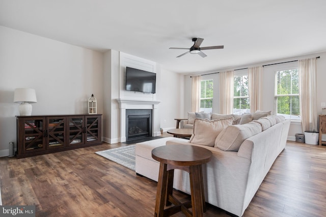 living area featuring a ceiling fan, wood finished floors, a fireplace with flush hearth, and baseboards