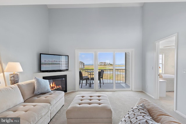living area featuring light colored carpet, baseboards, a towering ceiling, and a glass covered fireplace