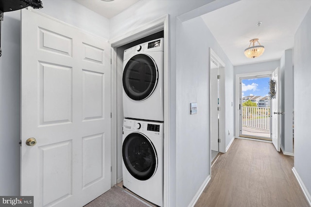 laundry room with stacked washer and dryer, baseboards, wood finished floors, and laundry area