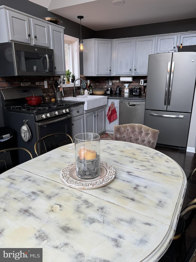 kitchen with appliances with stainless steel finishes, a sink, hanging light fixtures, light countertops, and tasteful backsplash