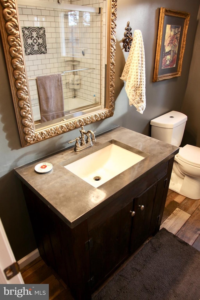 bathroom featuring wood finished floors, toilet, vanity, and a shower with door