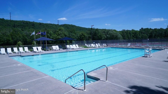 community pool with fence, a view of trees, and a patio area