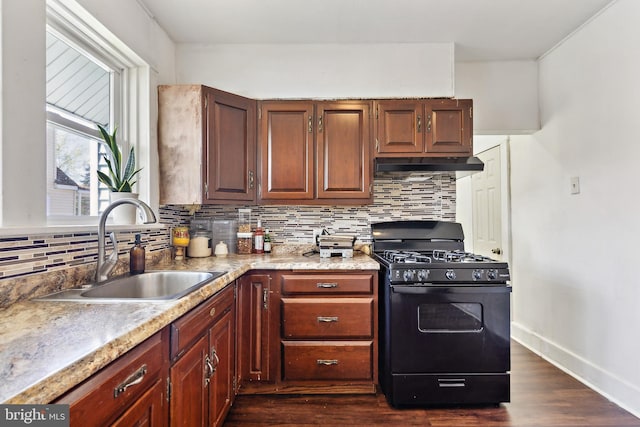 kitchen with under cabinet range hood, black gas range oven, backsplash, dark wood-style flooring, and a sink