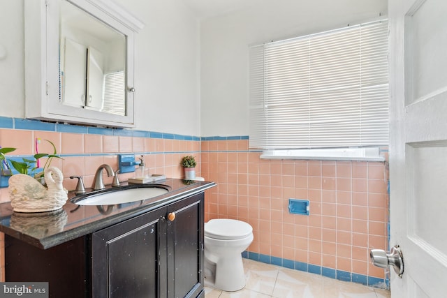 half bathroom with toilet, vanity, tile walls, and tile patterned floors