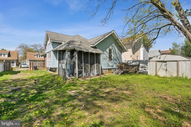 rear view of property with an outbuilding, a storage shed, fence, a yard, and a sunroom