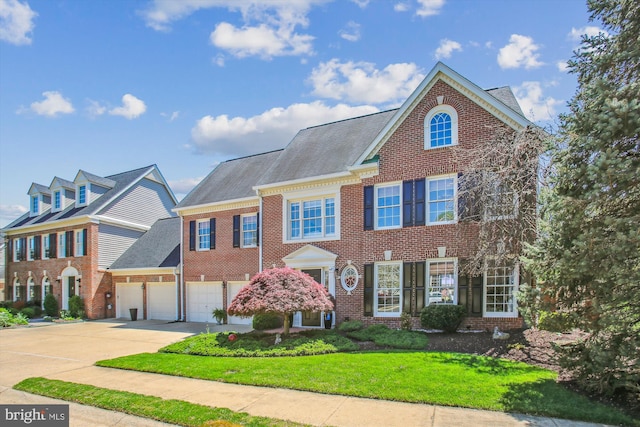 colonial-style house featuring concrete driveway, a front yard, a shingled roof, and brick siding